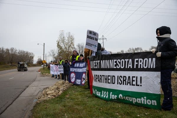 People hold signs and banners in a driveway