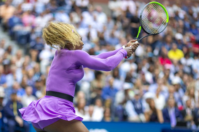 Serena Williams swinging a tennis racket on the court wearing a purple outfit.