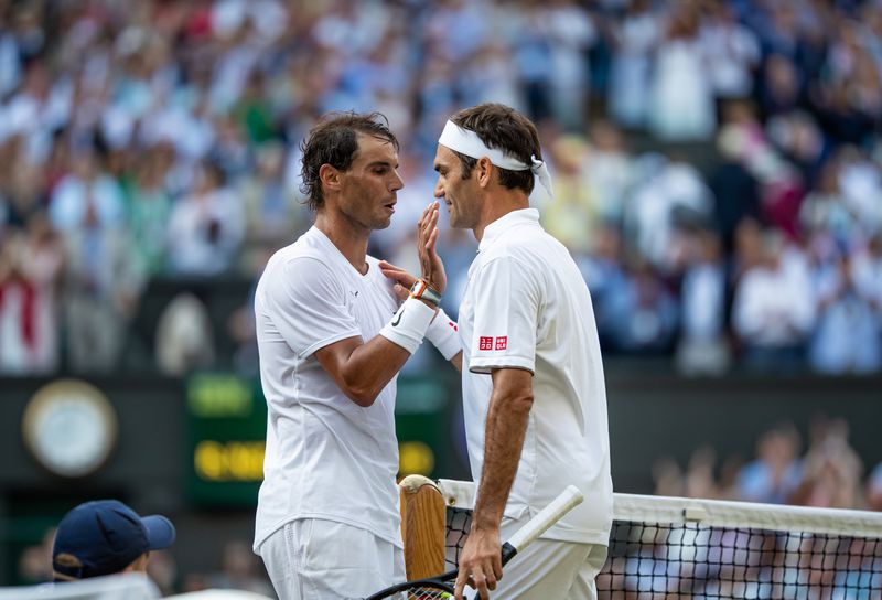 Nadal and Federer, both dressed in white, stand face-to-face. Federer lays a hand on Nadal’s shoulder.