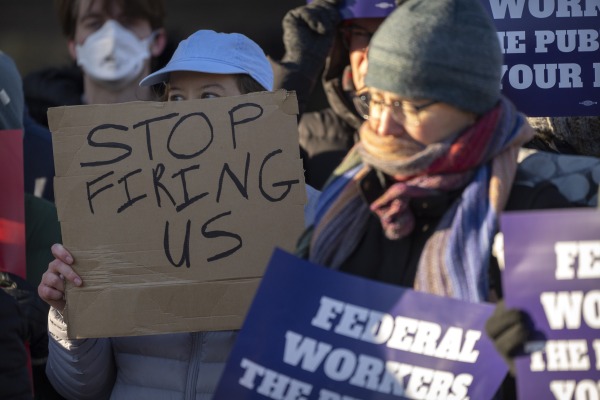 Demonstrators hold signs including one reading "stop firing us."