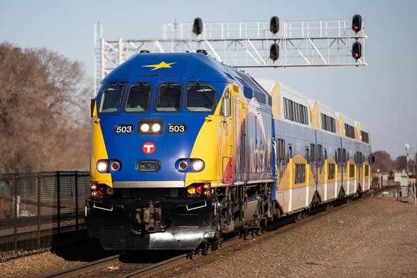 A blue and yellow train approaches a station.