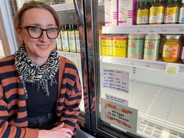 A woman stands near a grocery fridge display.