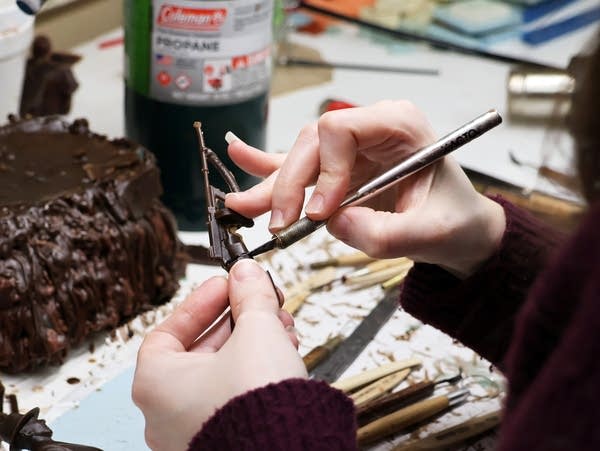 a woman uses a knife to carve a wax figure