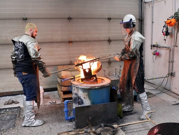 two people lift a bucket of molten metal