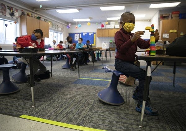 Kids wearing face masks sit at tables in a classroom. 