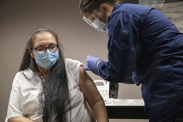 A woman wearing a face mask receives a vaccine.