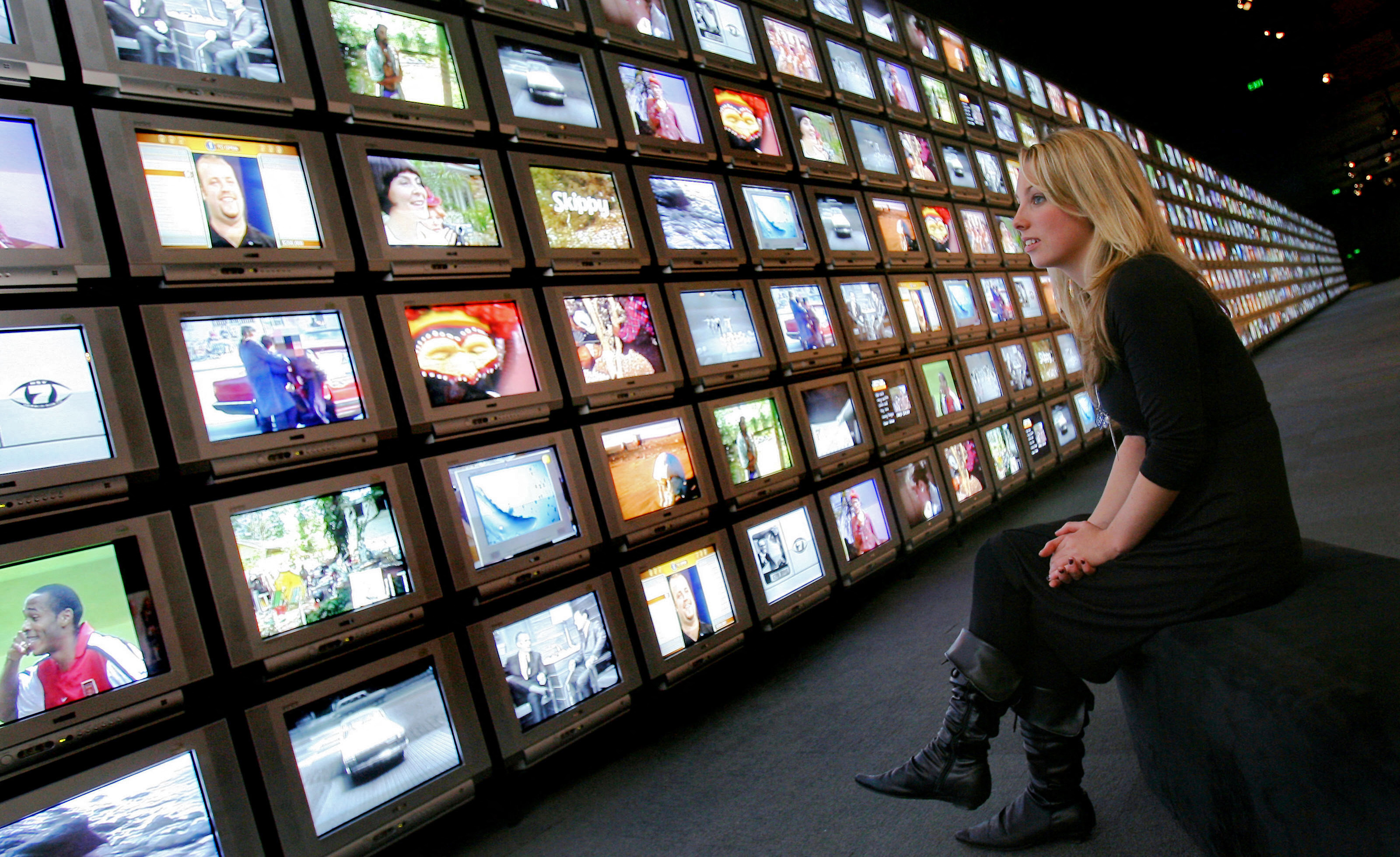 A woman looks at a wall of TV screens.