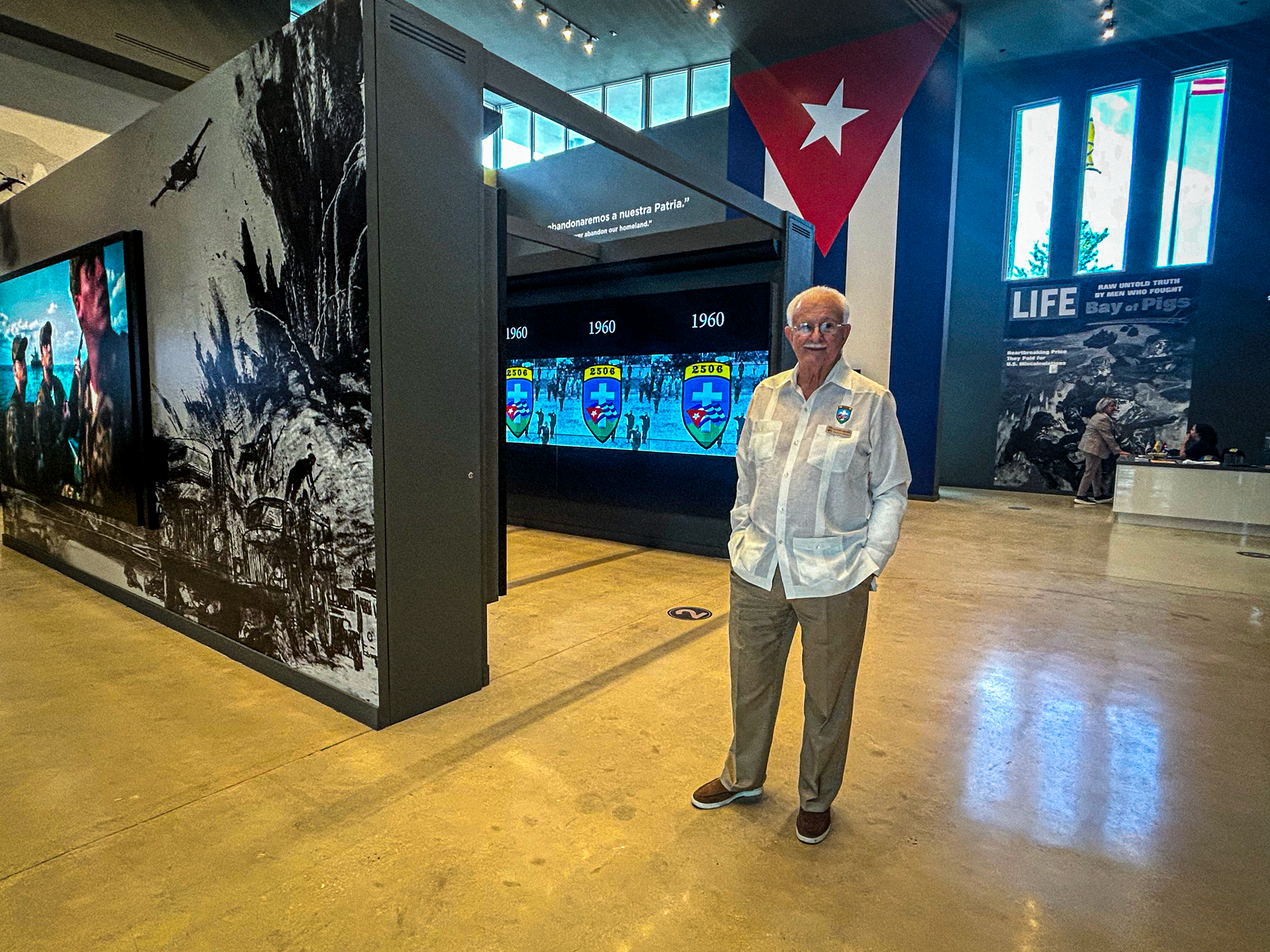 An elderly man stands amid walls with digital museum displays.