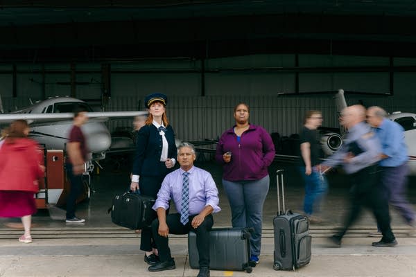 Three people pose outside of an airplane hangar.