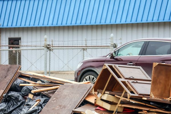 A maroon car is parked next to a pile of broken furniture and wood debris.
