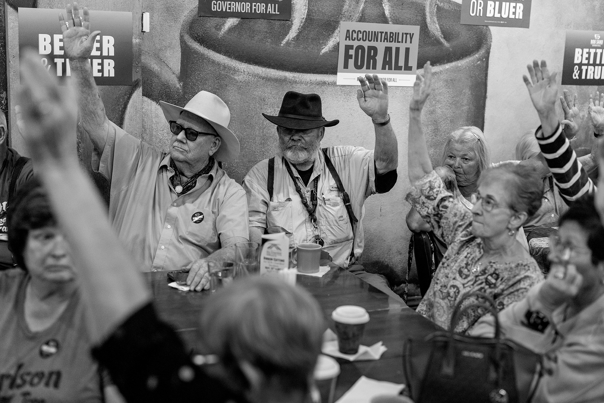 Group of people sitting around a table with their hands raised.