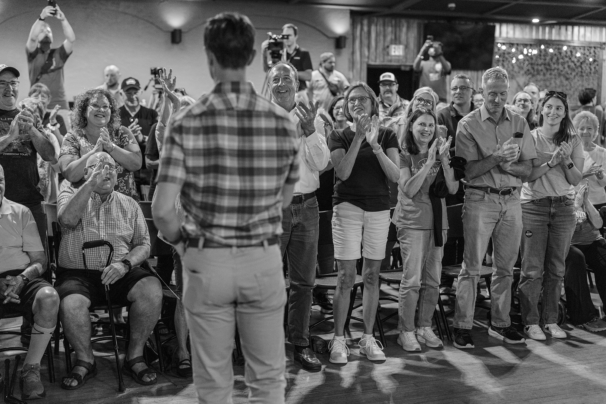 Crowd stands, clapping in front of Rob Sand, whose back is turned.