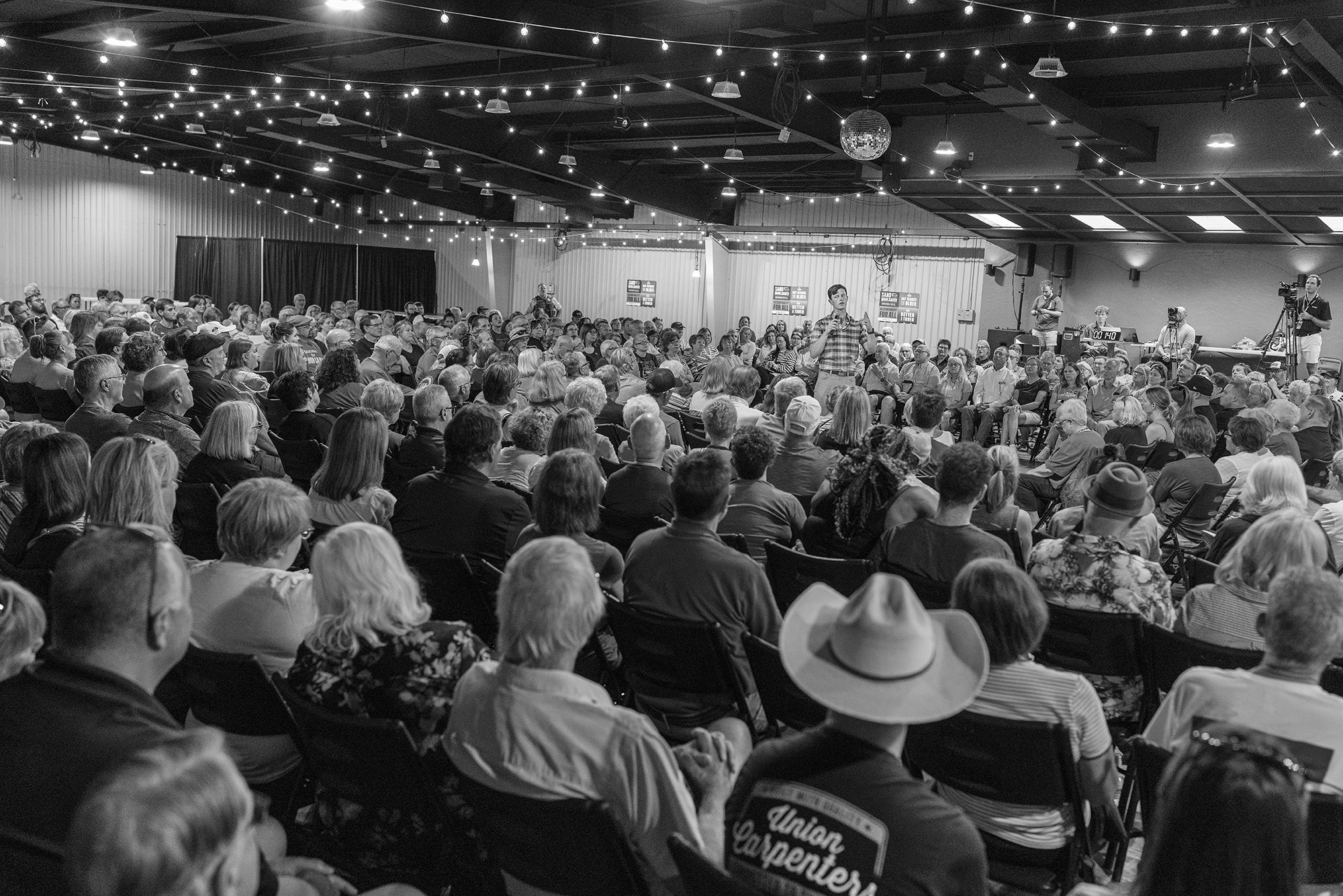 Rob Sand stands among a large crowd of seated people.