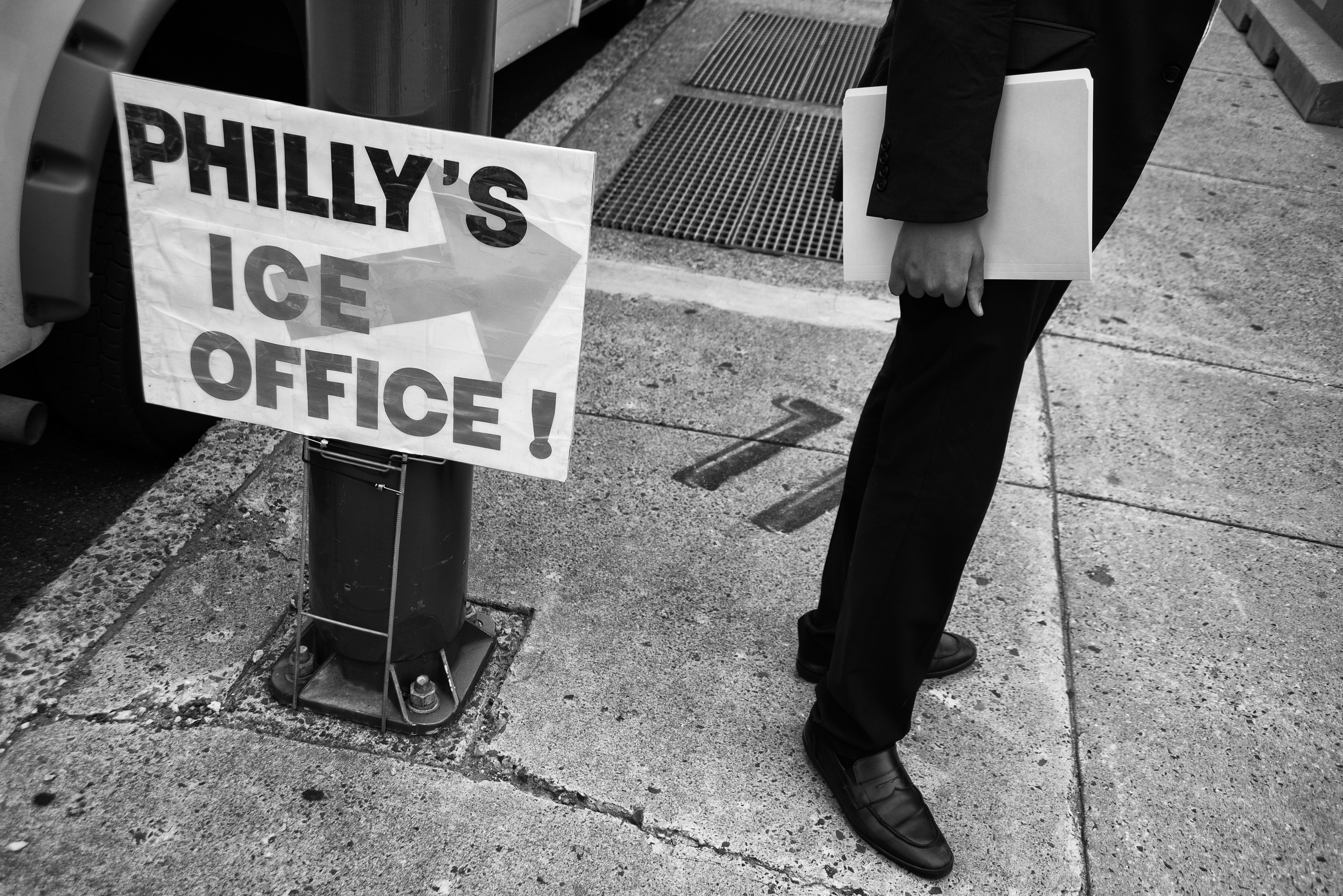Person standing next to a sign that reads "Philly's ICE Office."