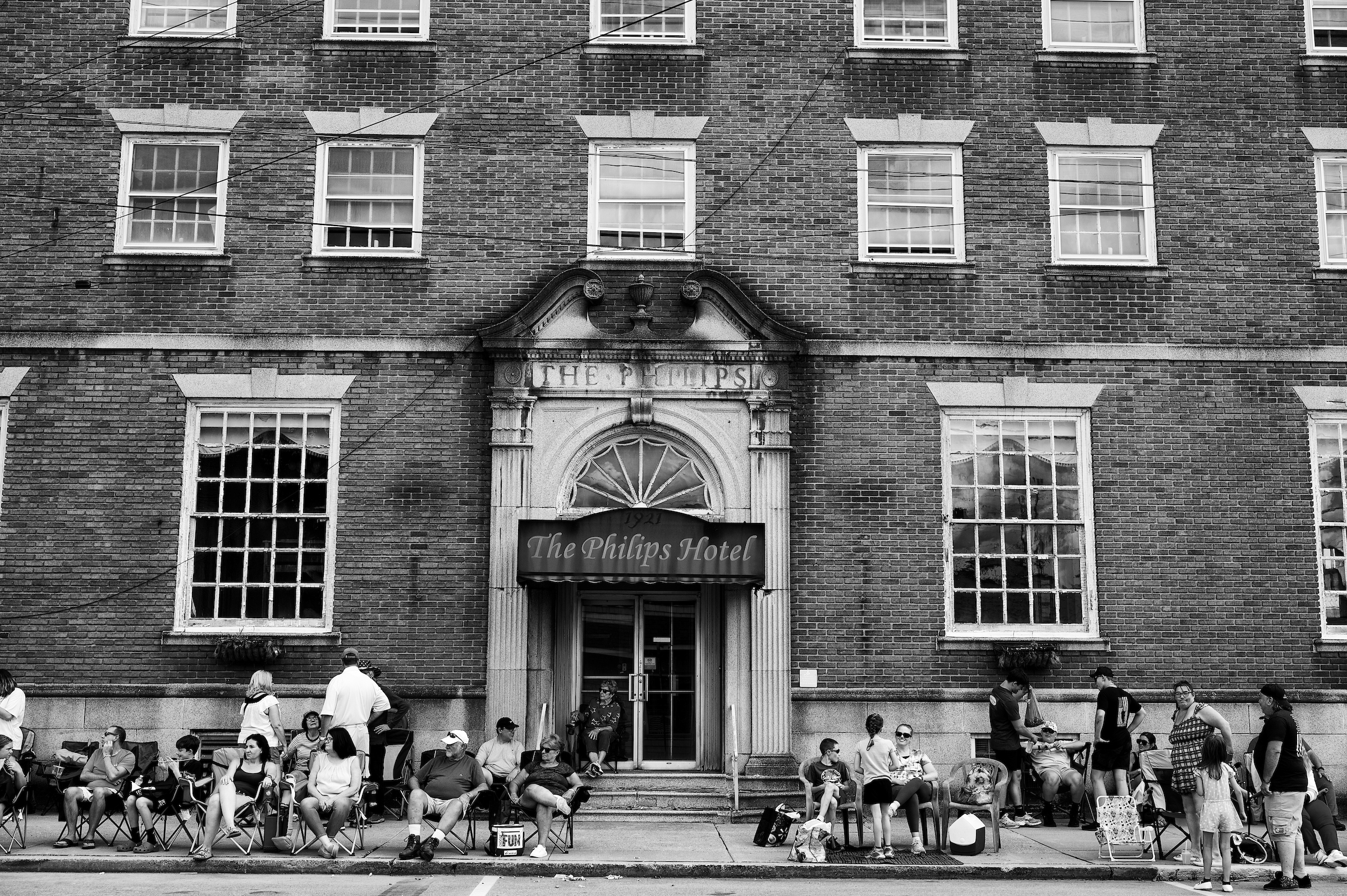 People sitting in chairs lining a small downtown street.