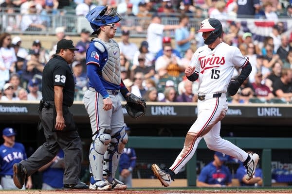 A baseball player runs into home plate while the catcher stands upright.