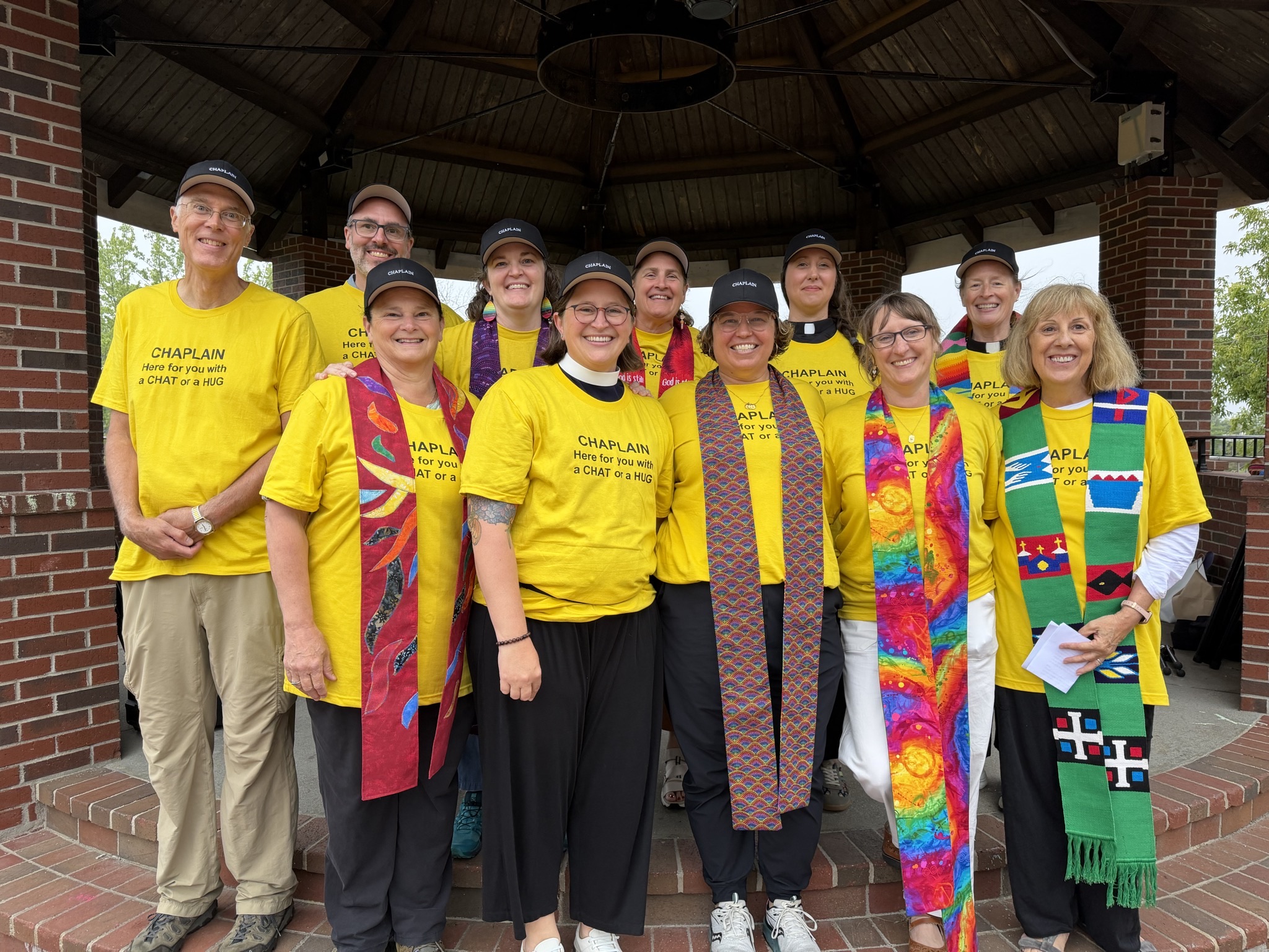 A group of religious leaders smiling and wearing shirts that read "CHAPLAIN here with you for a chat or a hug"