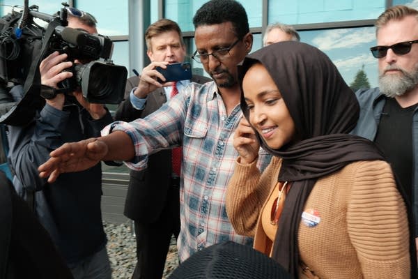 Ilhan Omar leaves, surrounded by cameras.