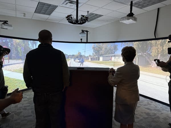 Two politicians are seen in silhouette in front of a large simulator screen.