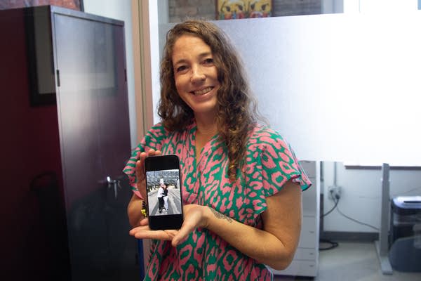 A smiling woman holds her phone which depicts a photo of a couple