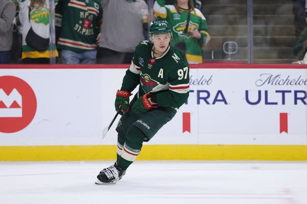A Wild hockey player in a green uniform skates on the ice.