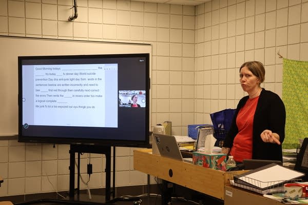 A woman teaches to a class with a document projected on a screen.