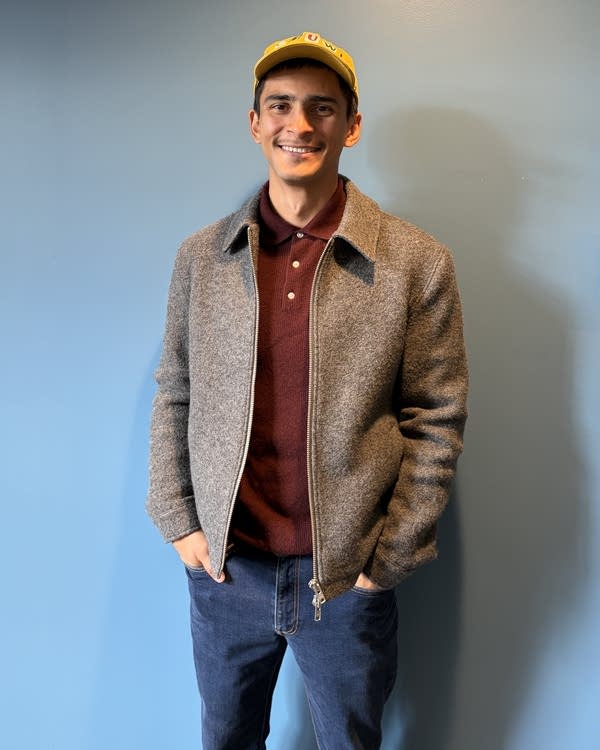 A man stands in front of a blue wall. 