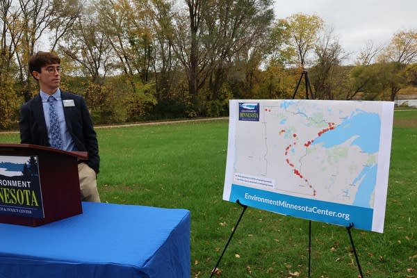 A man stands near a map set up in a green space outdoors. 