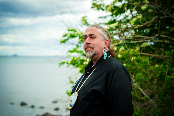 A man stands near a lakeshore background for a portrait photo.