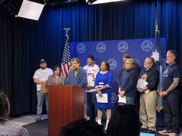 A group stands behind a podium as one person speaks to press.