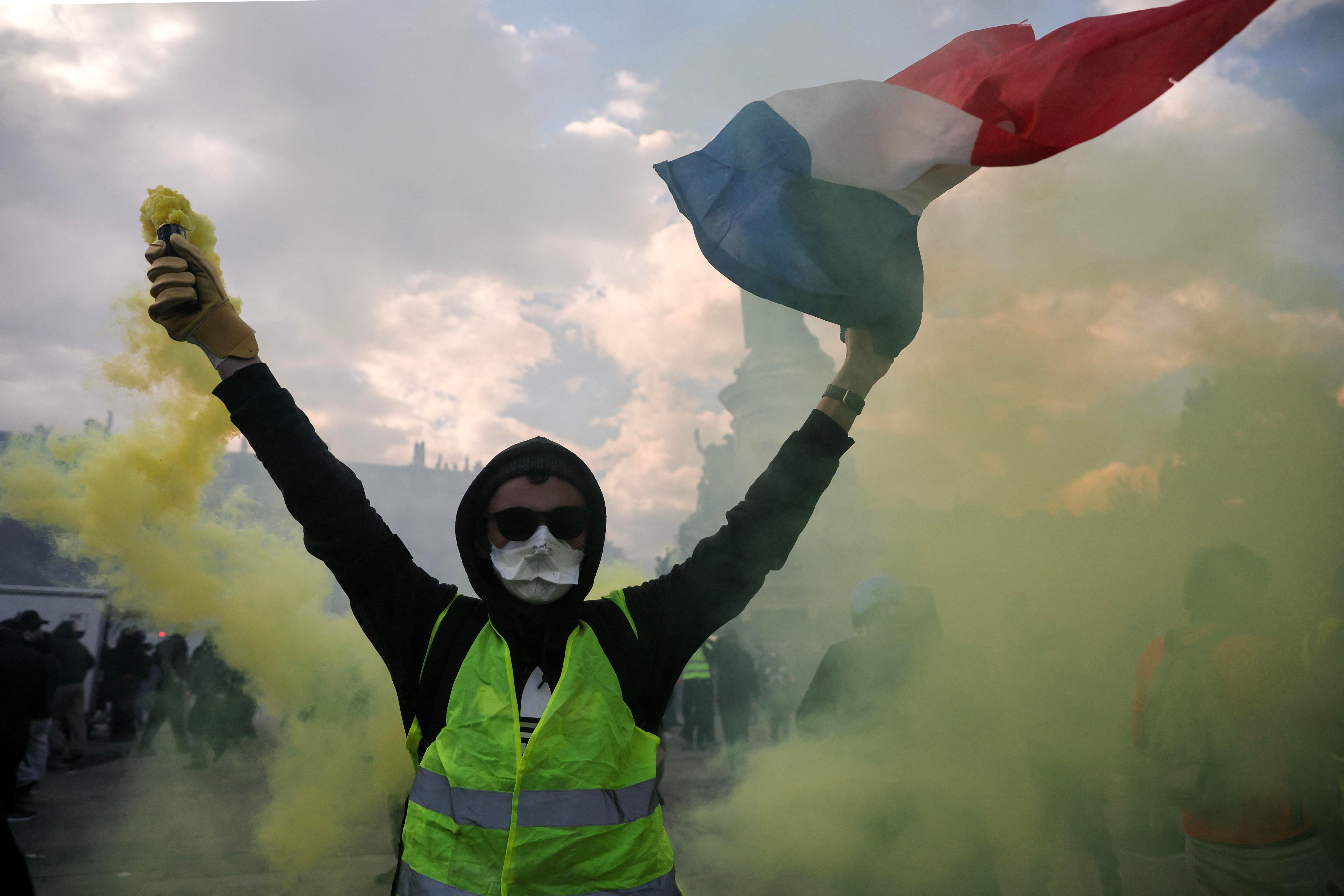 A masked protester holding a smoke flare and French flag