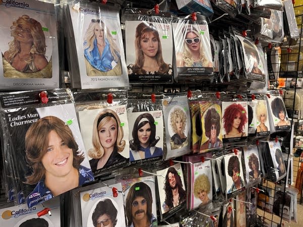 A collection of wigs hangs on a rack of a costume shop.